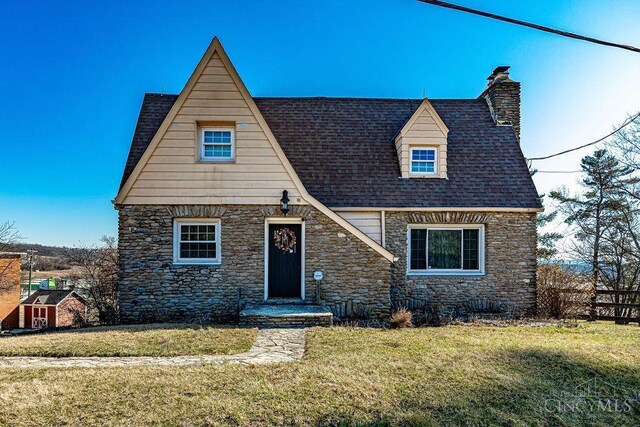 view of front of home featuring stone siding, a chimney, a front yard, and roof with shingles