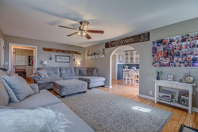 living area featuring a textured wall, arched walkways, wood-type flooring, and ceiling fan