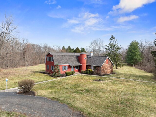 view of front of property with a front lawn, a gambrel roof, roof with shingles, and a chimney