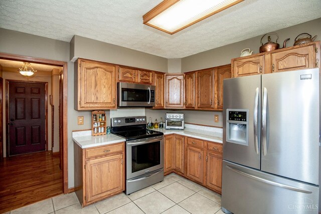 343 Whiteoak Dr, Wilmington, OH 45177 - kitchen with appliances with stainless steel finishes, light countertops, light tile patterned floors, a textured ceiling, and brown cabinetry