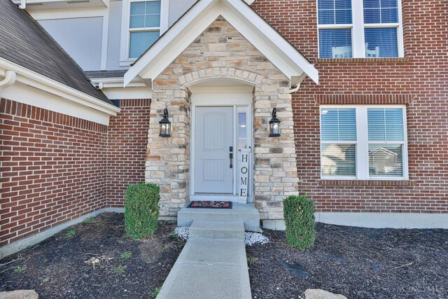 property entrance with brick siding, stone siding, and a shingled roof