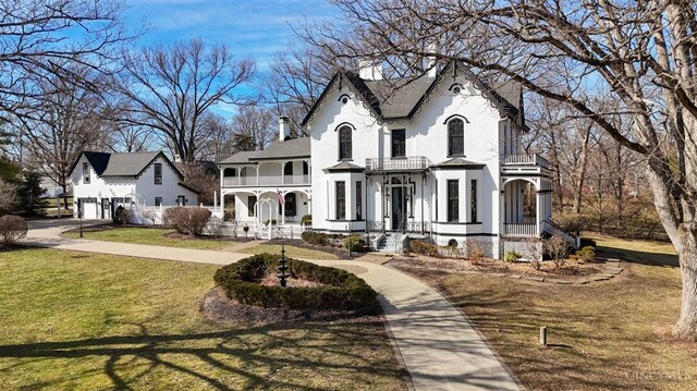 french country home featuring a balcony, a chimney, and a front yard