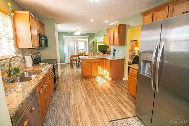kitchen featuring backsplash, a sink, light wood-style floors, a peninsula, and appliances with stainless steel finishes