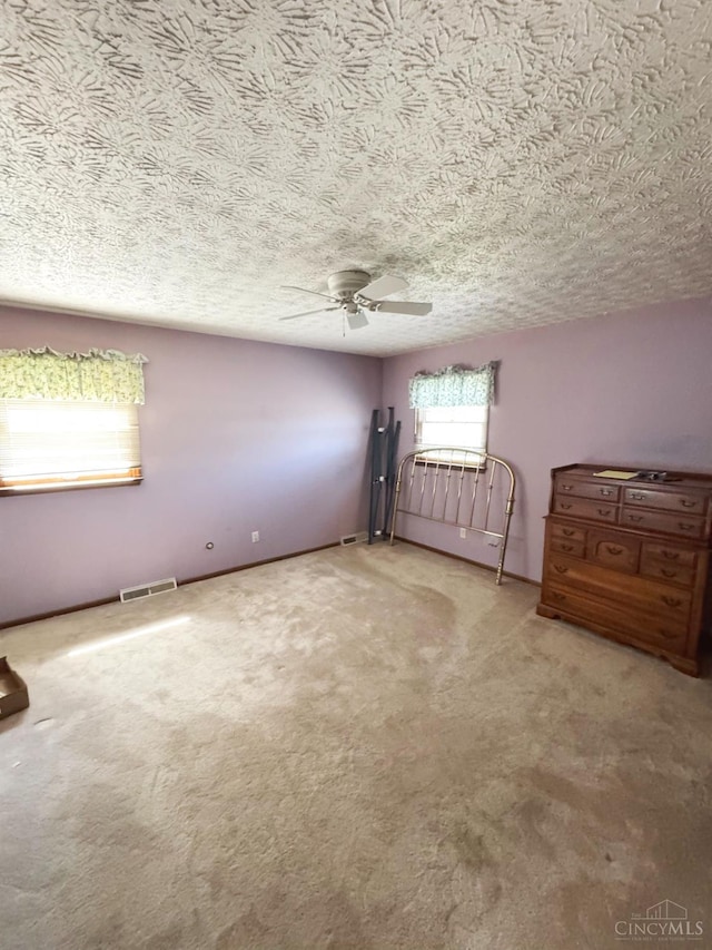 unfurnished bedroom featuring ceiling fan, a textured ceiling, carpet flooring, and visible vents