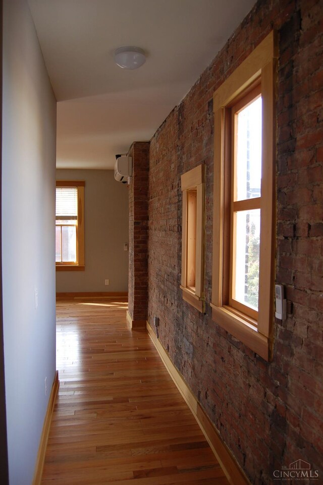 hallway with a wall mounted air conditioner, plenty of natural light, brick wall, and wood finished floors