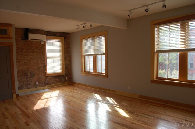 spare room featuring brick wall, light wood finished floors, a wall unit AC, and a healthy amount of sunlight