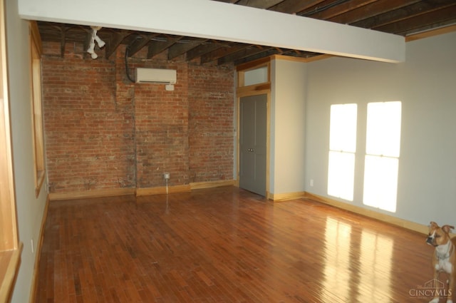 unfurnished room with brick wall, wood finished floors, baseboards, and a wall mounted air conditioner