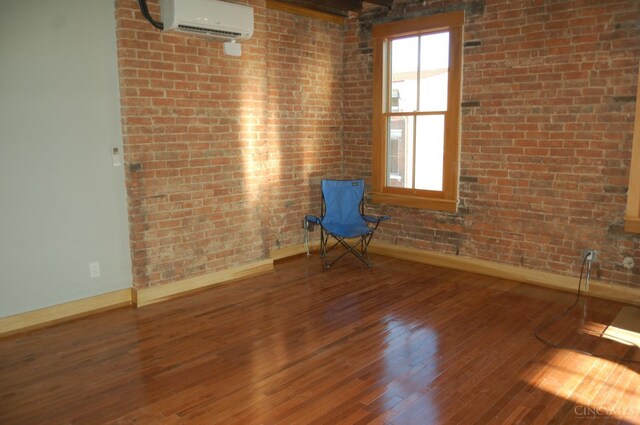 unfurnished room with baseboards, a wall mounted AC, hardwood / wood-style floors, and brick wall