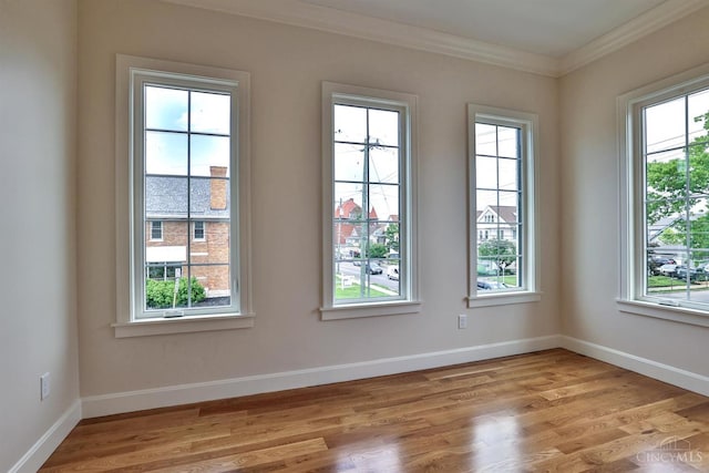 unfurnished room with crown molding, plenty of natural light, light wood-type flooring, and baseboards