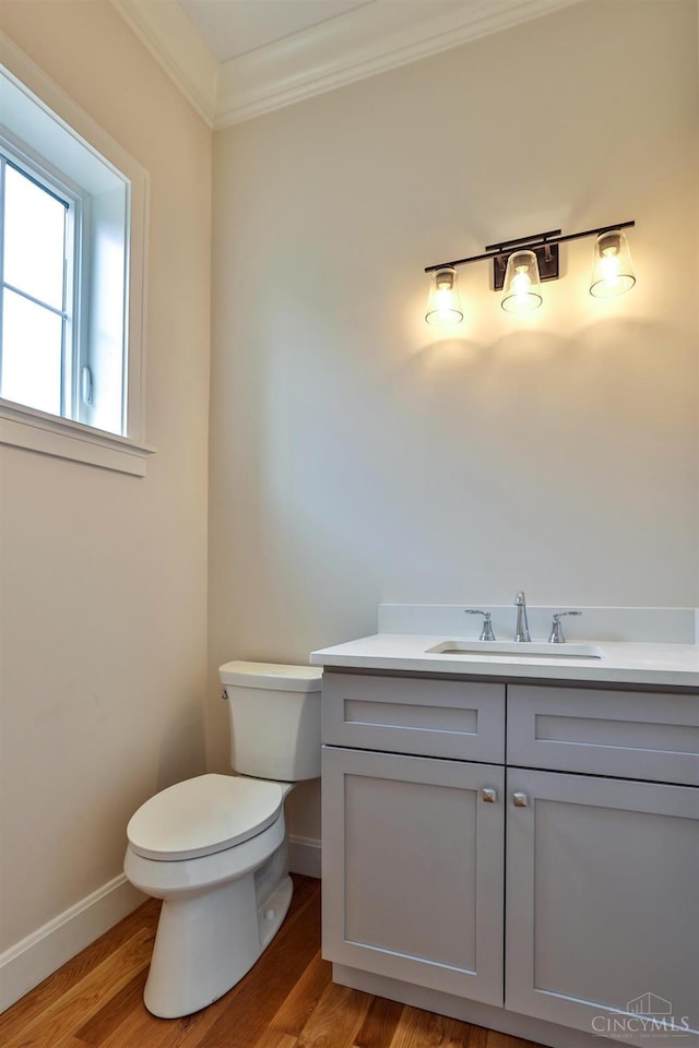 half bath with wood finished floors, toilet, baseboards, vanity, and crown molding