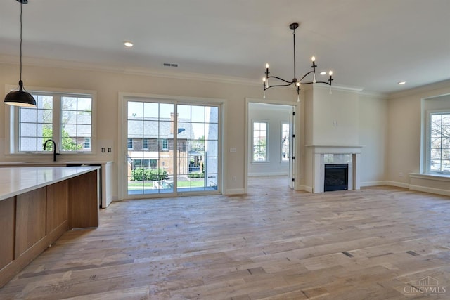 unfurnished living room with plenty of natural light, a chandelier, light wood-type flooring, ornamental molding, and baseboards