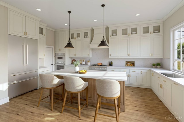 kitchen featuring built in refrigerator, a sink, custom range hood, a center island, and light countertops