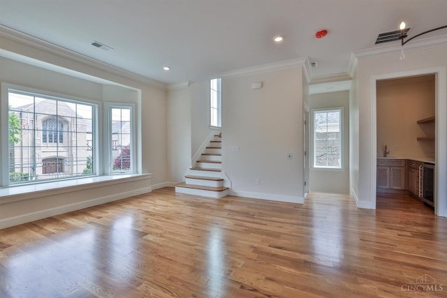 unfurnished room featuring ornamental molding, beverage cooler, healthy amount of natural light, stairway, and light wood finished floors