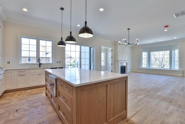 kitchen with a chandelier, ornamental molding, light wood-type flooring, a kitchen island, and light countertops