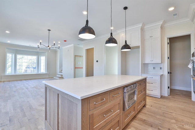kitchen with ornamental molding, light wood finished floors, stainless steel microwave, white cabinetry, and light countertops