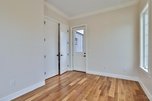 spare room featuring plenty of natural light, ornamental molding, light wood-style floors, and baseboards