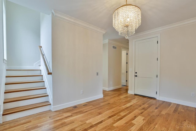 spare room with a chandelier, ornamental molding, light wood-type flooring, baseboards, and stairway