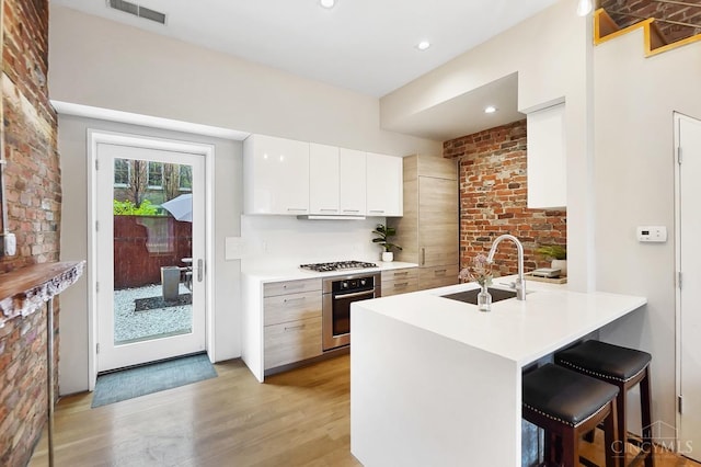 kitchen with visible vents, a sink, appliances with stainless steel finishes, a kitchen breakfast bar, and light wood-style flooring