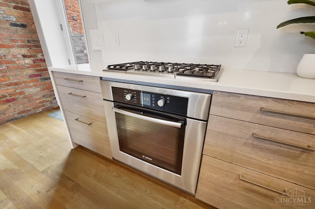 kitchen featuring light countertops, appliances with stainless steel finishes, light wood finished floors, and brick wall