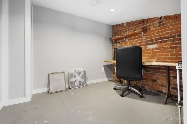 unfurnished office with concrete floors, baseboards, and brick wall