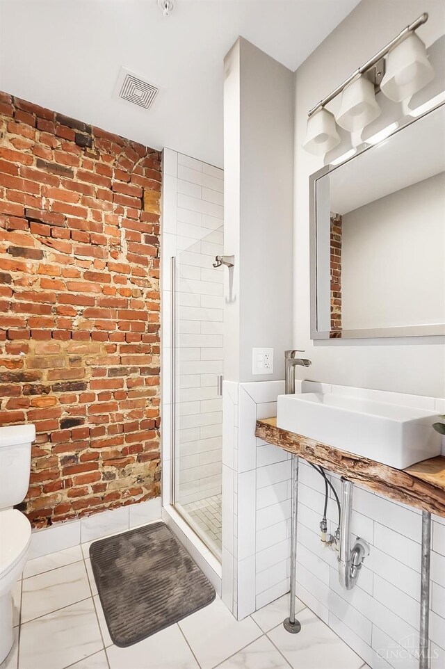 bathroom featuring a shower stall, visible vents, toilet, a sink, and brick wall