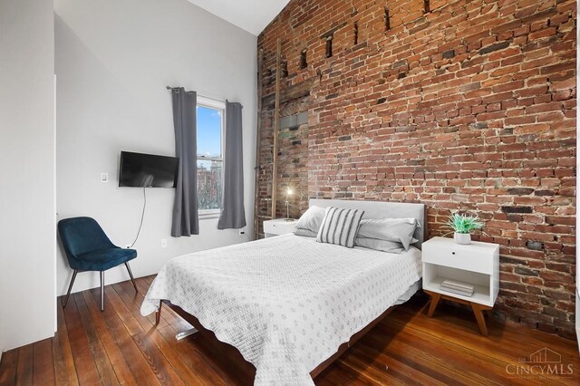 bedroom with brick wall, dark wood-style flooring, and high vaulted ceiling