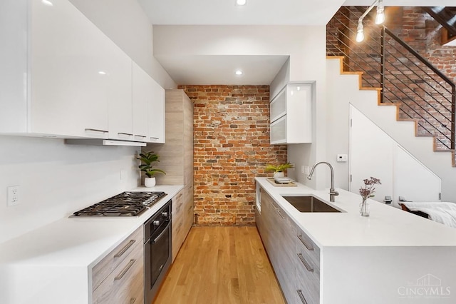 kitchen featuring brick wall, modern cabinets, a sink, and appliances with stainless steel finishes