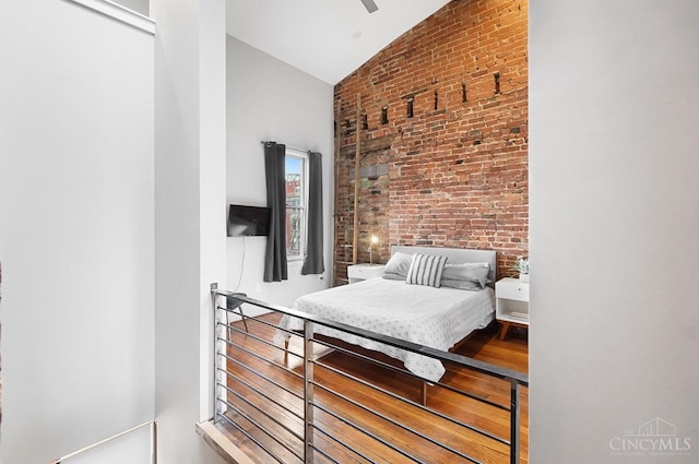 bedroom featuring brick wall, high vaulted ceiling, and wood finished floors