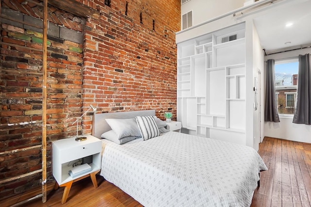 bedroom with brick wall and hardwood / wood-style flooring