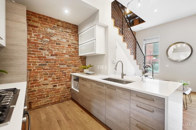 kitchen featuring a peninsula, light countertops, a sink, brick wall, and light wood finished floors