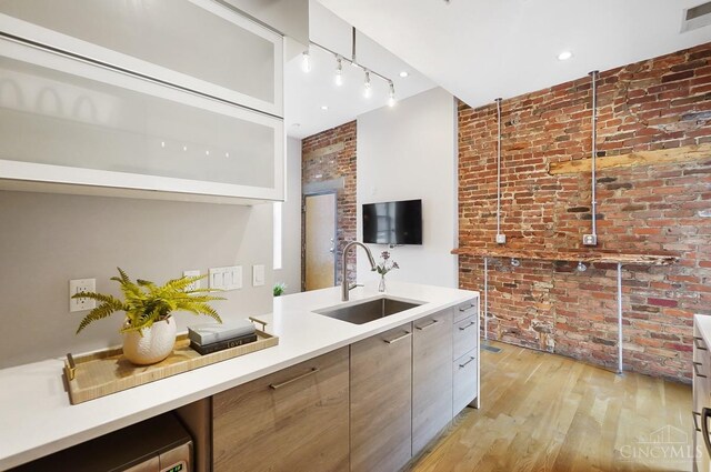 kitchen with a sink, light wood finished floors, brick wall, and modern cabinets
