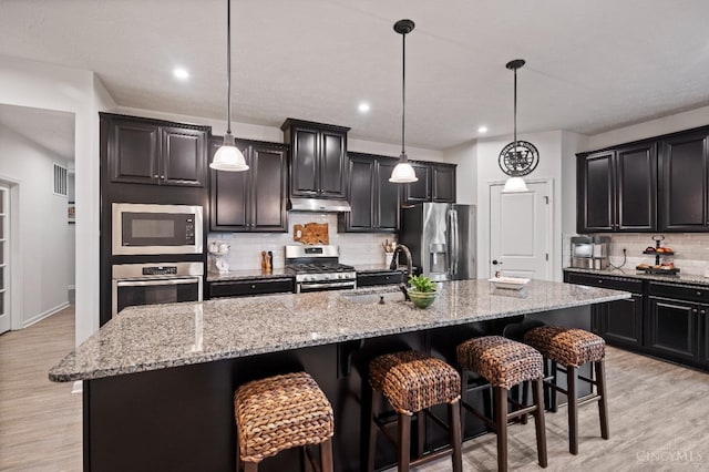 1113 Clover Field Dr, Miami Twp, OH 45140 - kitchen with a sink, a breakfast bar, under cabinet range hood, stainless steel appliances, and decorative backsplash