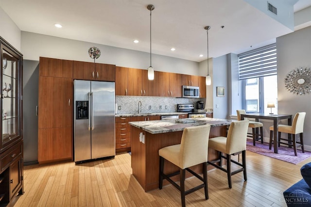 kitchen featuring appliances with stainless steel finishes, a kitchen breakfast bar, a kitchen island, a sink, and light wood-type flooring