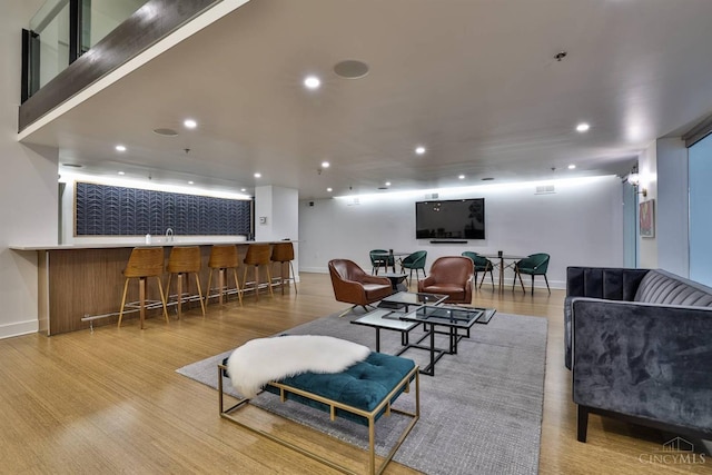 living room with bar with sink, wood finished floors, baseboards, and recessed lighting