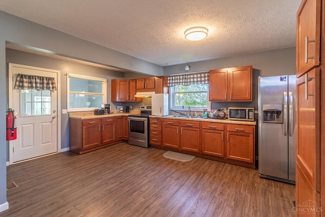 819 E Main St, West Union, OH 45693 - kitchen with appliances with stainless steel finishes, brown cabinets, under cabinet range hood, dark wood finished floors, and a textured ceiling