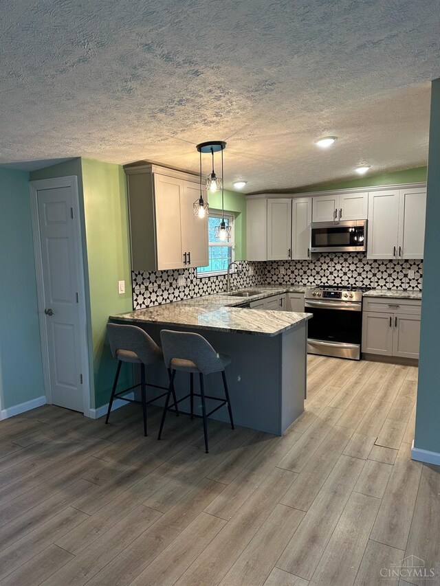 41 Wolfer Dr, Batavia Twp, OH 45102 - kitchen featuring light wood-style flooring, appliances with stainless steel finishes, decorative backsplash, and a peninsula