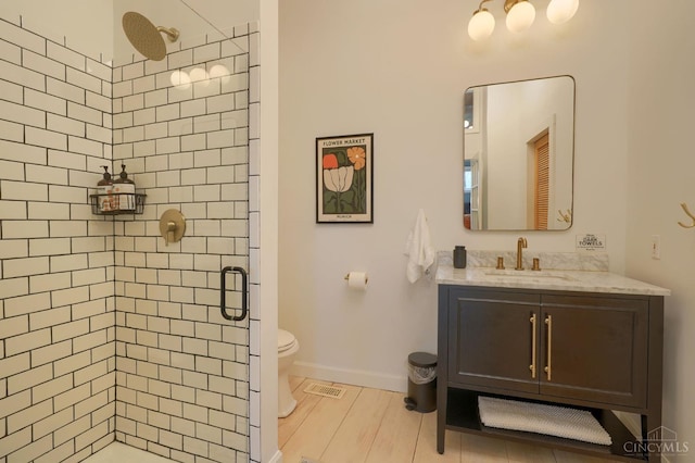 bathroom with wood finished floors, toilet, vanity, baseboards, and a stall shower