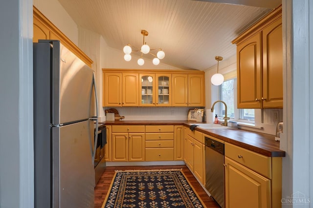 kitchen featuring butcher block countertops, a sink, stainless steel appliances, lofted ceiling, and dark wood finished floors
