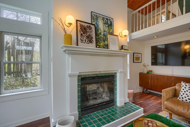 living area featuring a towering ceiling, a tile fireplace, wood finished floors, and baseboards