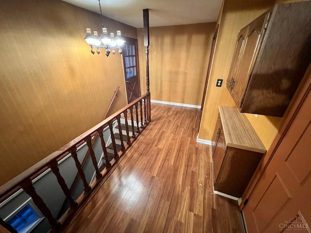 staircase with baseboards, wood finished floors, and a notable chandelier
