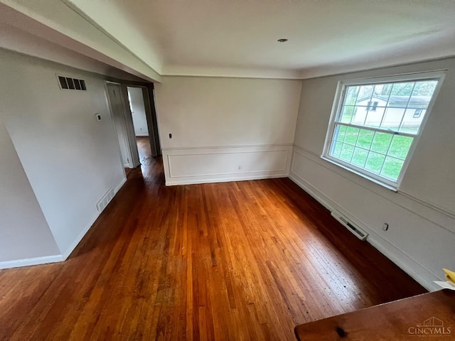 empty room featuring wood-type flooring, wainscoting, and visible vents