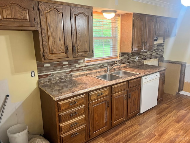 kitchen featuring a sink, backsplash, white dishwasher, and wood finished floors