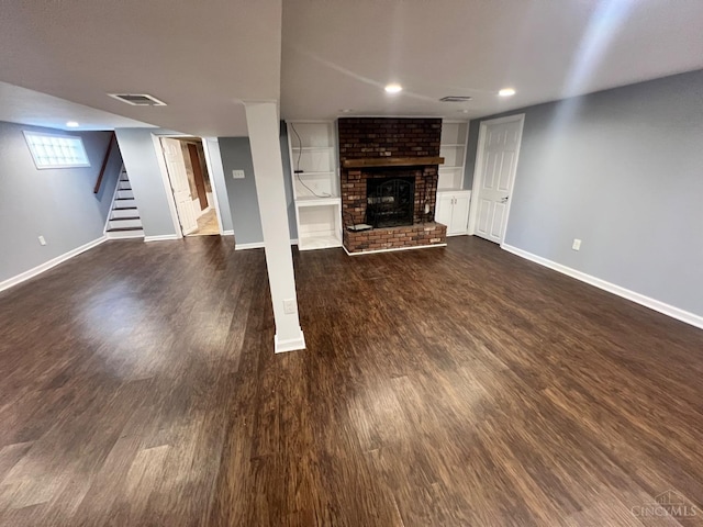 unfurnished living room featuring baseboards, visible vents, a brick fireplace, dark wood-type flooring, and stairway