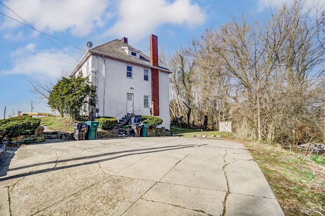 back of property featuring stairs, a chimney, and stucco siding