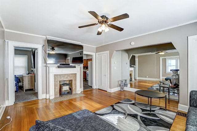 living room featuring baseboards, a ceiling fan, wood finished floors, and a tile fireplace