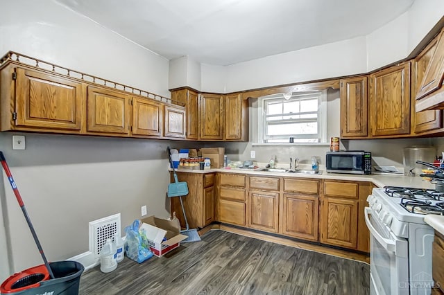 kitchen with white gas range oven, a sink, stainless steel microwave, visible vents, and brown cabinetry