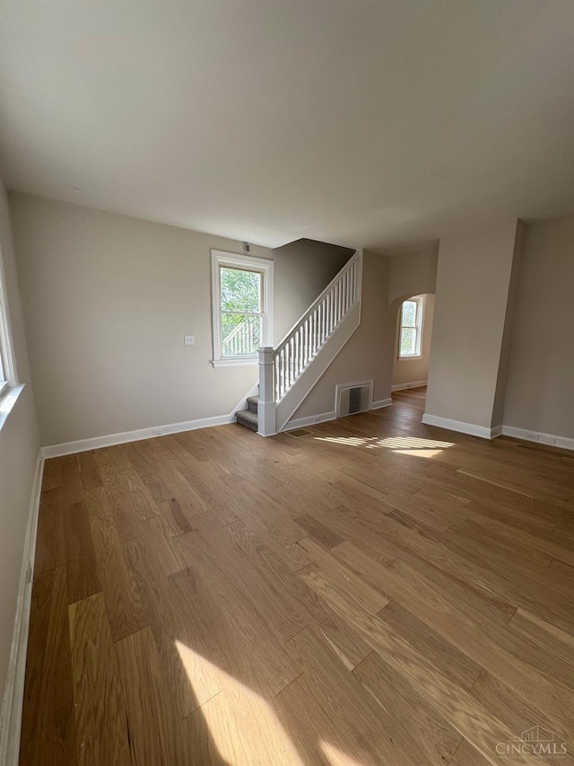 unfurnished living room featuring wood finished floors, visible vents, stairs, and a healthy amount of sunlight