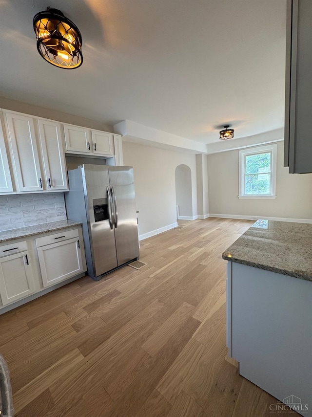kitchen featuring light wood-type flooring, arched walkways, white cabinets, and stainless steel fridge