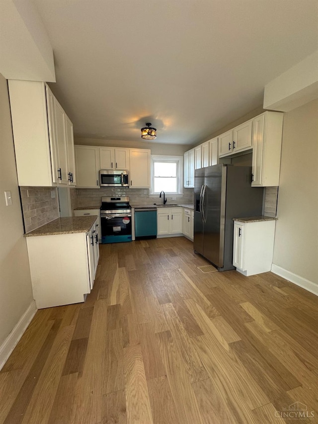 kitchen with white cabinets, stainless steel appliances, a sink, light wood-style flooring, and tasteful backsplash