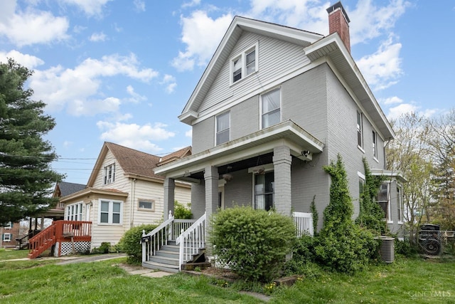 view of front of property featuring a chimney, covered porch, a front yard, and brick siding